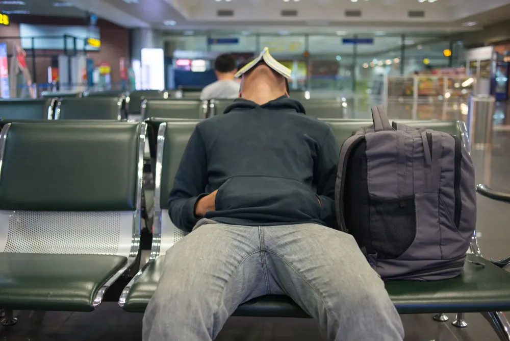 Person sleeping in airpot with a book propped on their face